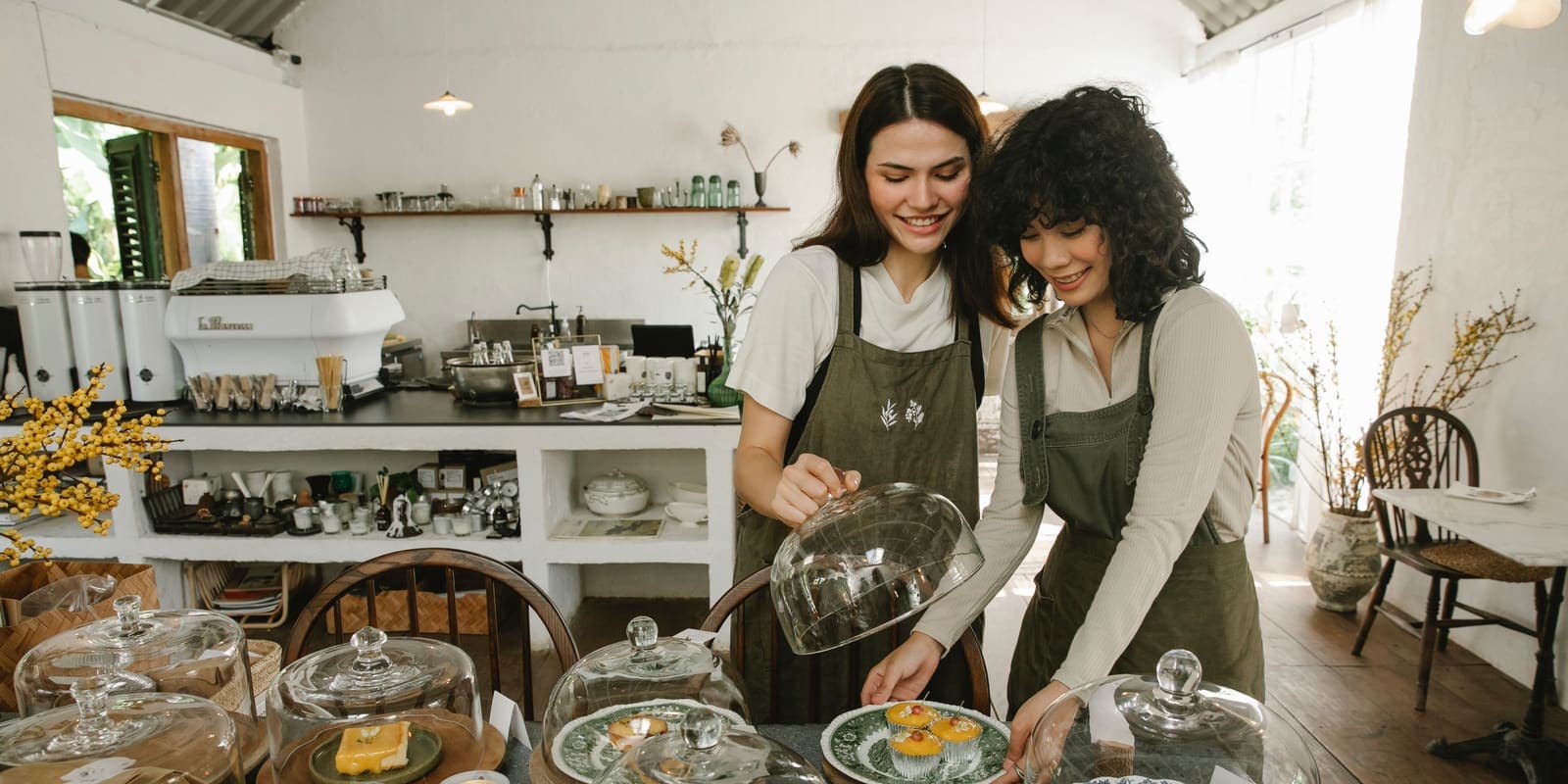 Two bakery owners setting out pastries under glass domes